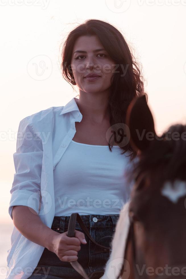 Woman in summer clothes enjoys riding a horse on a beautiful sandy beach at sunset. Selective focus photo