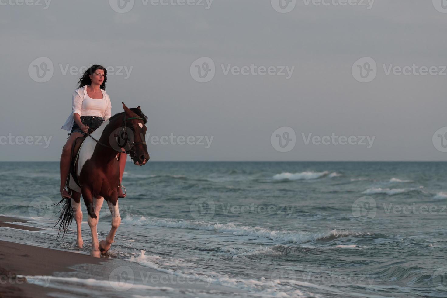 Woman in summer clothes enjoys riding a horse on a beautiful sandy beach at sunset. Selective focus photo