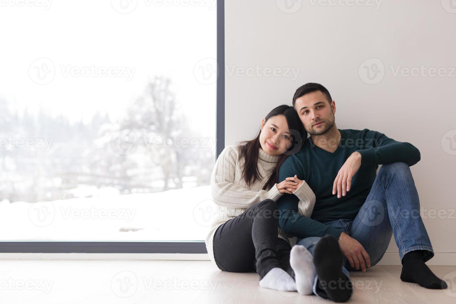 pareja multiétnica sentada en el suelo cerca de la ventana en casa foto