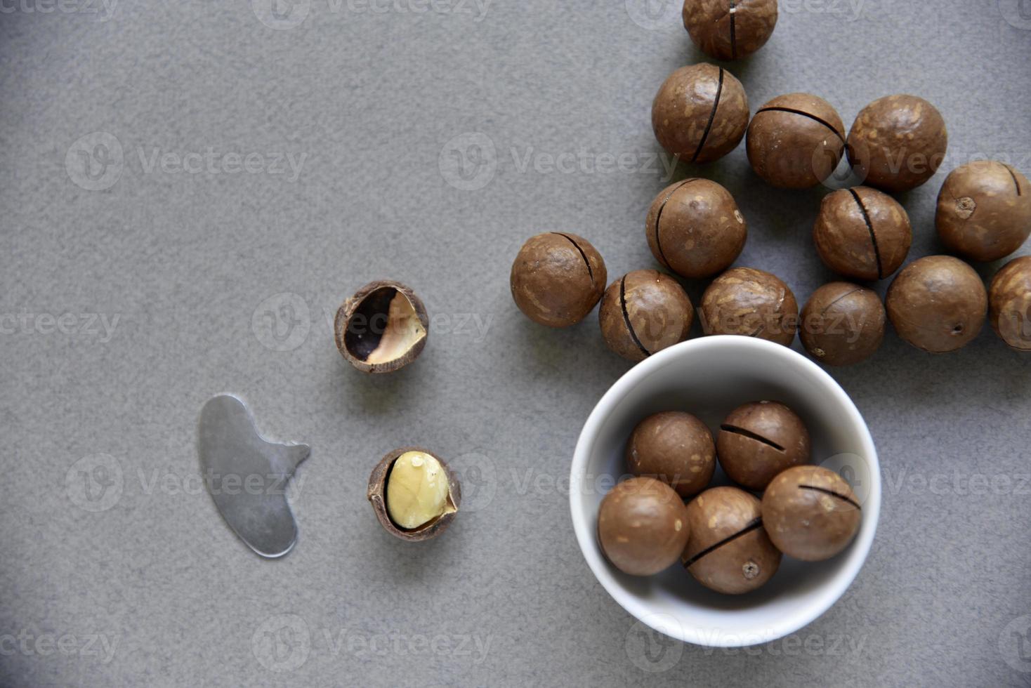 Macadamia nut in a dish with a bottle opener on a gray background. Macadamia nut prepared for use in a vase. Delicious breakfast of nuts. photo
