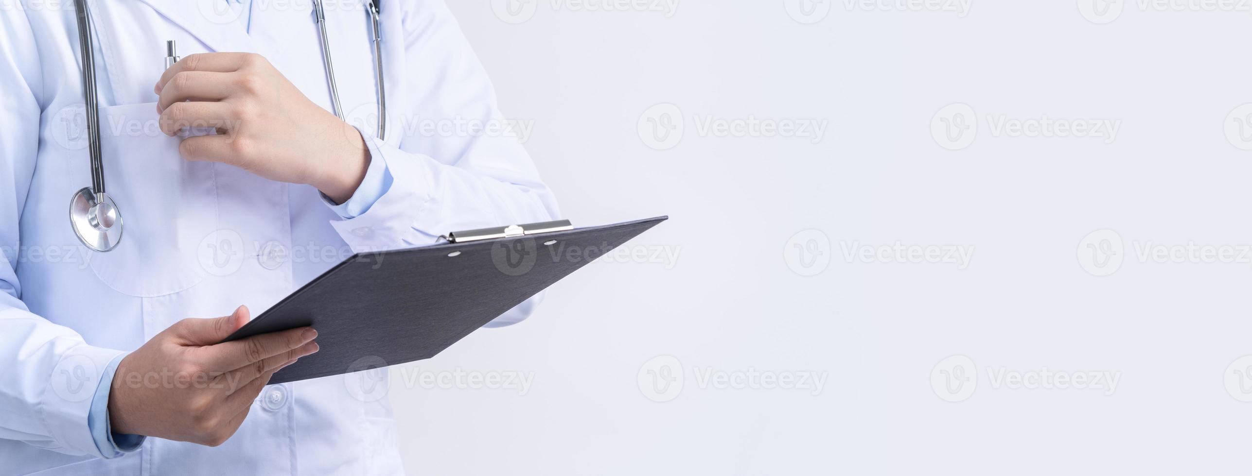 Doctor with stethoscope in white coat holding clipboard, writing medical record diagnosis, isolated on white background, close up, cropped view. photo