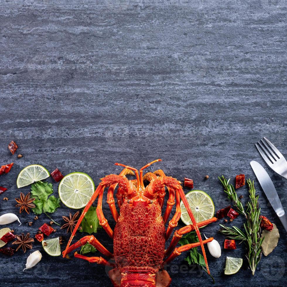 Cooked boiled lobster, delicious dinner seafood meal set with knife and fork on black stone slate background, restaurant menu design, top view, overhead photo