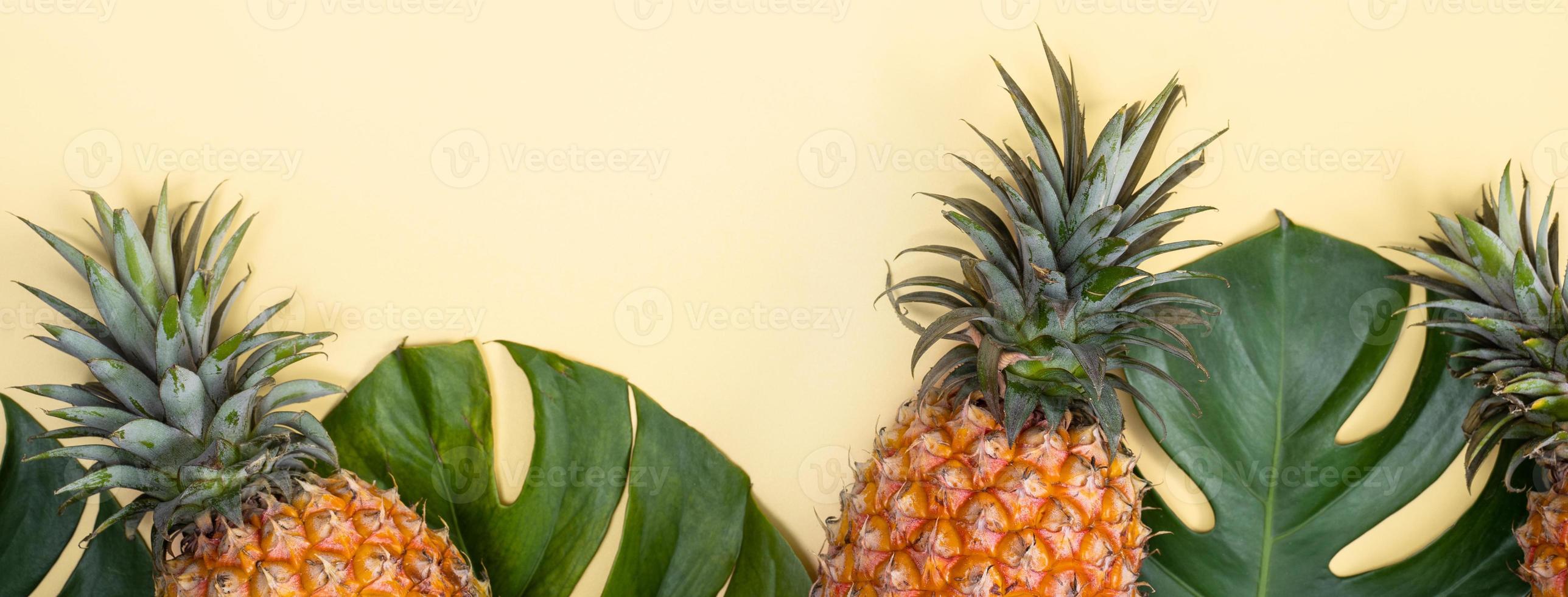 Beautiful pineapple on tropical palm monstera leaves isolated on bright pastel yellow background, top view, flat lay, overhead above summer fruit. photo