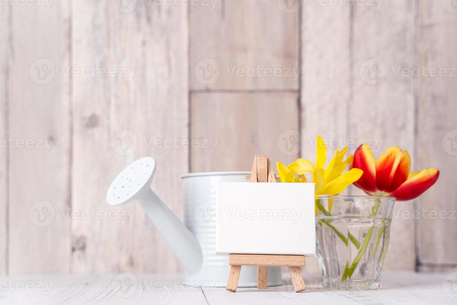 Tulip flower arrangement in glass vase with heart greeting, watering can decor on wooden table background wall, close up, Mother's Day design concept. photo