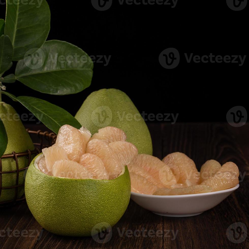 Fresh pomelo, pummelo, grapefruit, shaddock on wooden table over black background, close up, copy space. Fruit for Mid-autumn festival. photo