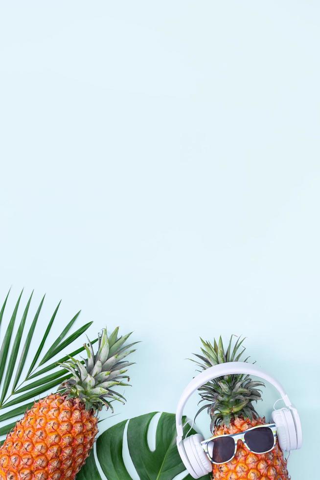 Funny pineapple wearing white headphone, concept of listening music, isolated on colored background with tropical palm leaves, top view, flat lay design. photo