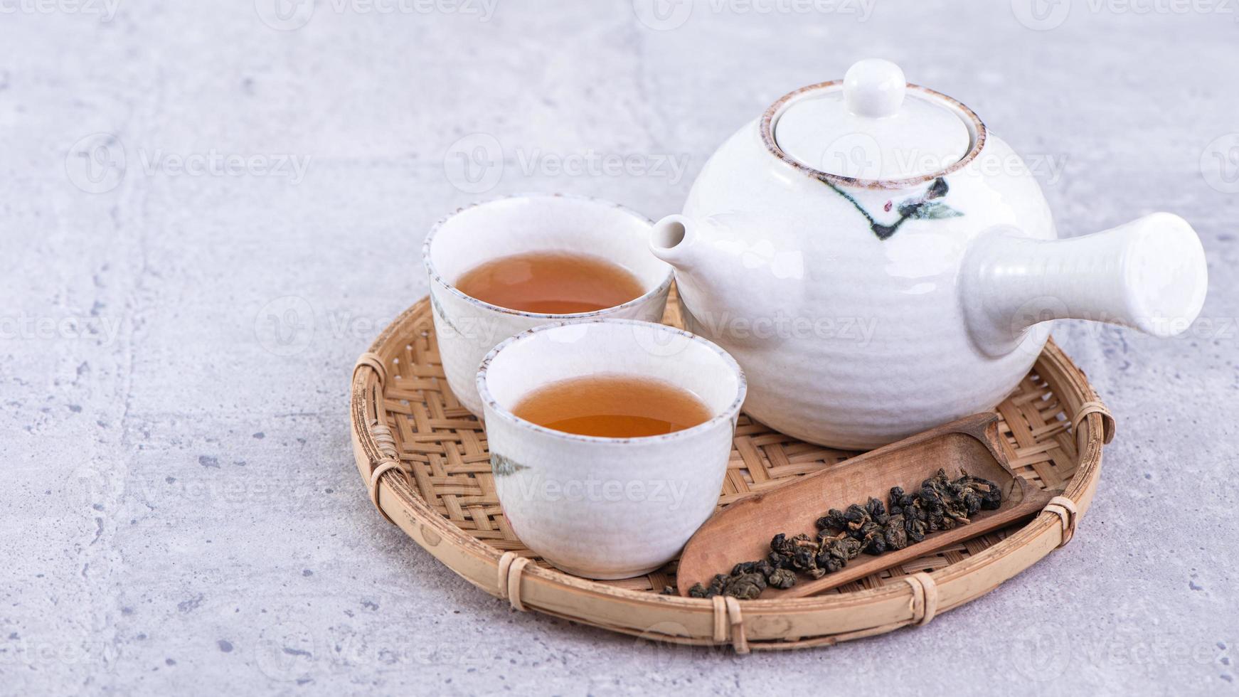 Hot tea in white teapot and cups on a sieve over bright gray cement background, closeup, copy space design concept. photo