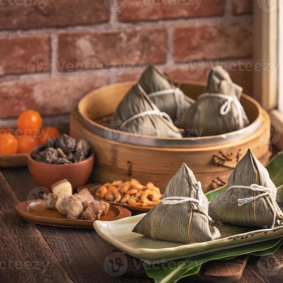 Rice dumpling - Chinese zongzi food in a steamer on wooden table with red brick wall, window background at home for Dragon Boat Festival concept, close up. photo