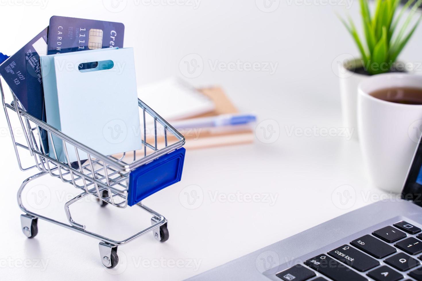 pago en línea de la oficina, compras en casa, pago electrónico con concepto de tarjeta de crédito, computadora portátil en el fondo de la mesa blanca con carrito de compras, primer plano. foto