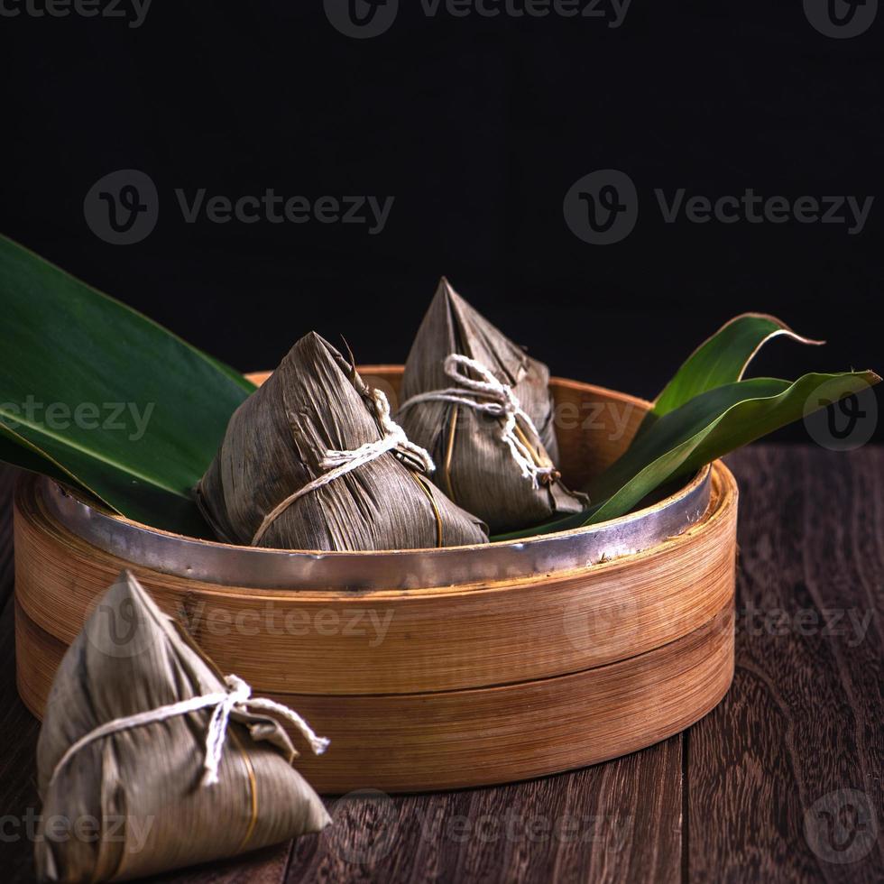 bola de arroz, zongzi - montón de comida tradicional china cocinada en una mesa de madera sobre fondo negro, concepto de festival de botes de dragón, primer plano, espacio de copia foto