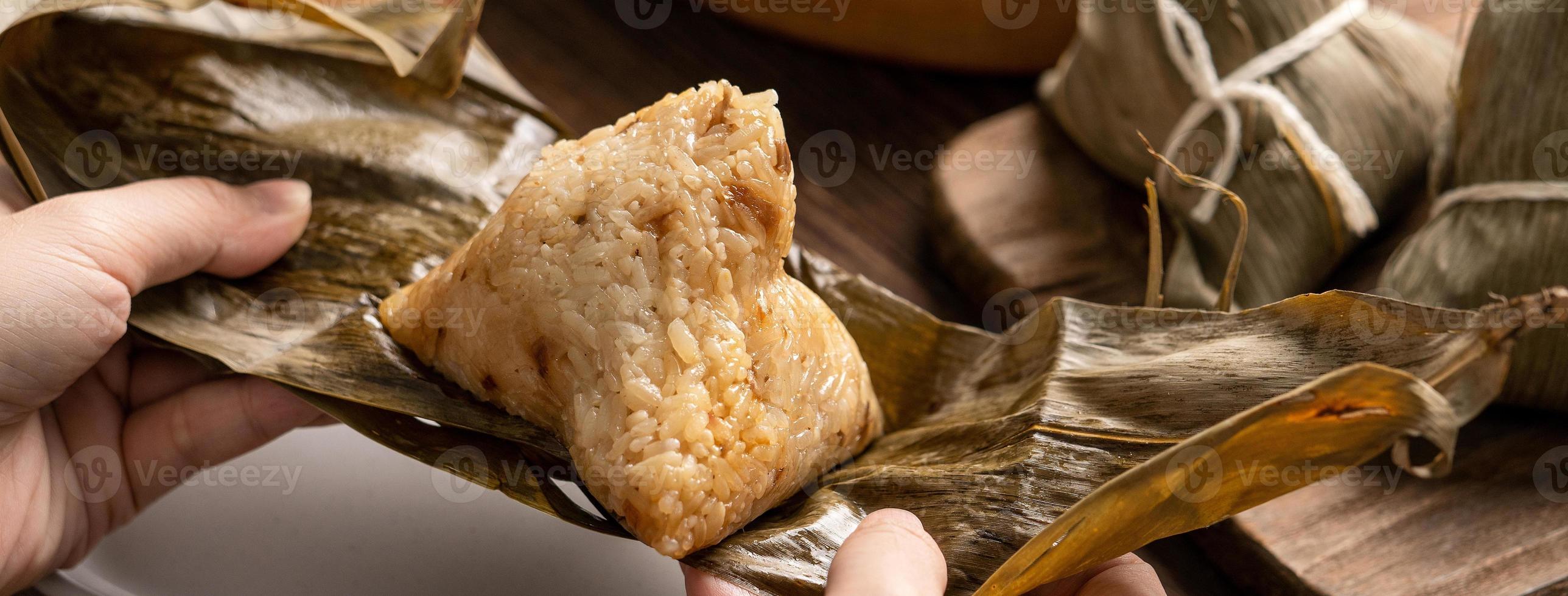 Rice dumpling zongzi eating - Young Asian woman is eating Chinese traditional food on wooden table at home for Dragon Boat Festival celebration, close up photo