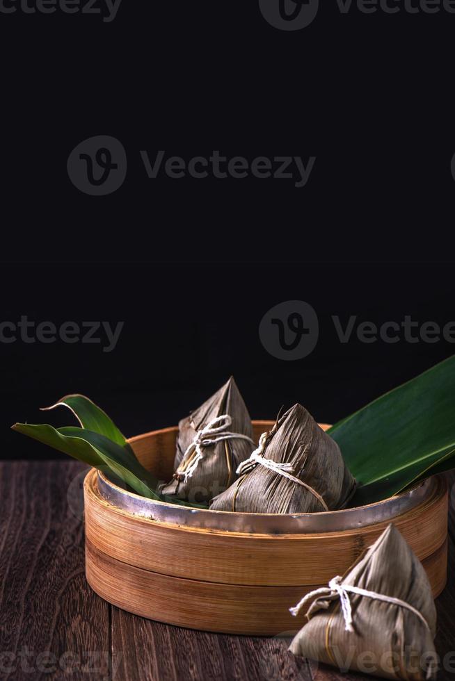 Zongzi - Chinese rice dumpling zongzi in a steamer on wooden table black retro background for Dragon Boat Festival celebration, close up, copy space. photo