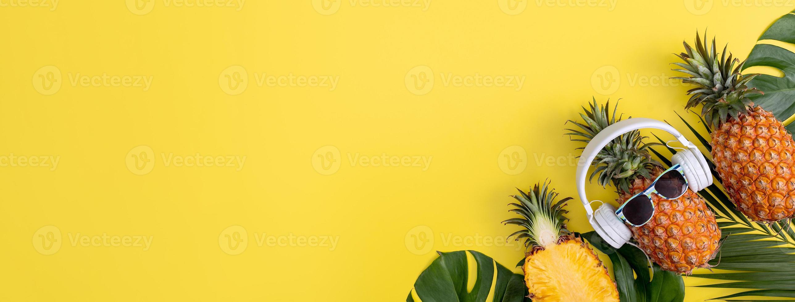 Funny pineapple wearing white headphone, listen music, isolated on yellow background with tropical palm leaves, top view, flat lay design concept. photo