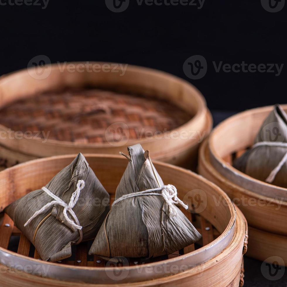 Rice dumpling, zongzi - Dragon Boat Festival, Bunch of Chinese traditional cooked food in steamer on wooden table over black background, close up, copy space photo