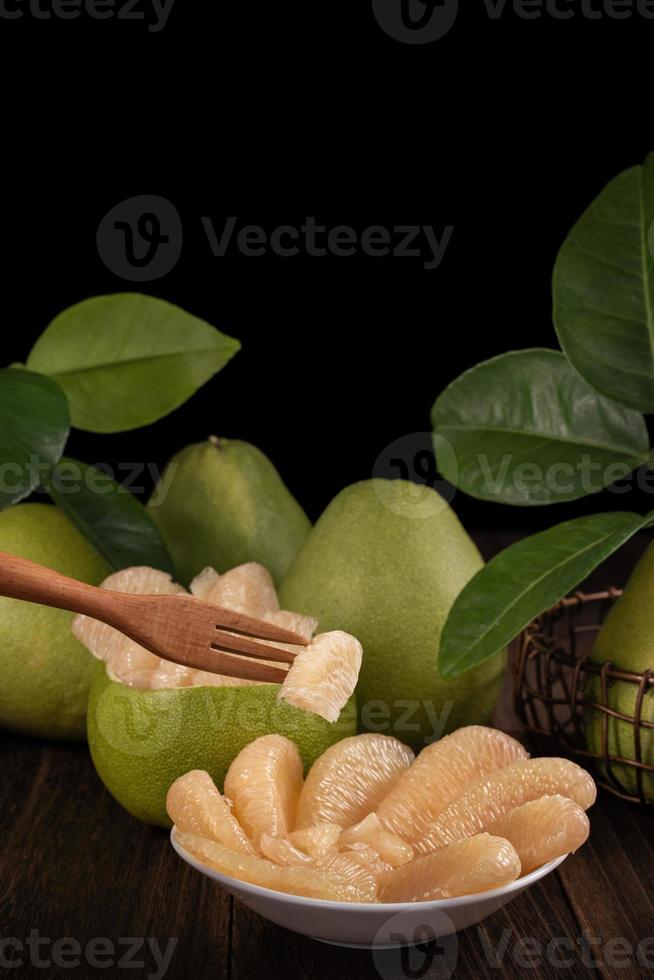 Fresh pomelo, pummelo, grapefruit, shaddock on wooden table over black background, close up, copy space. Fruit for Mid-autumn festival. photo