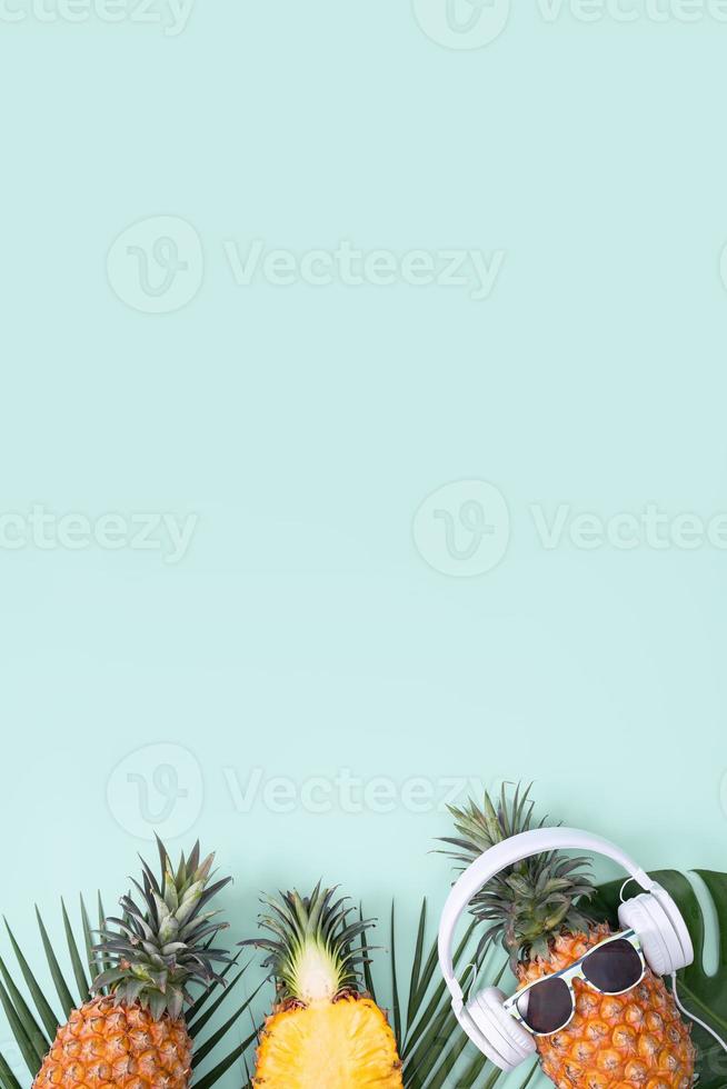 Funny pineapple wearing white headphone, concept of listening music, isolated on colored background with tropical palm leaves, top view, flat lay design. photo