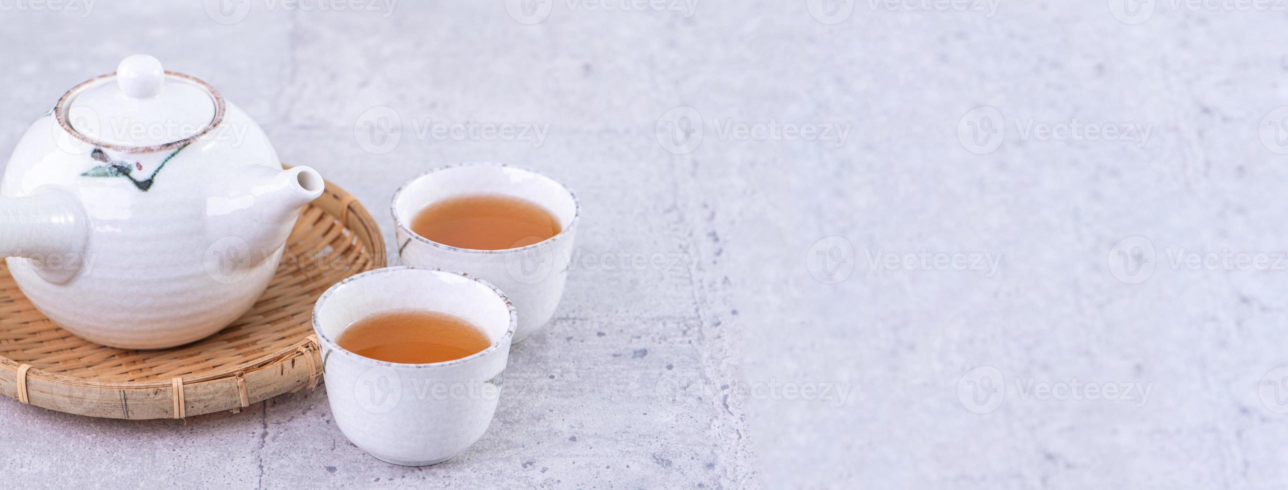 Hot tea in white teapot and cups on a sieve over bright gray cement background, closeup, copy space design concept. photo