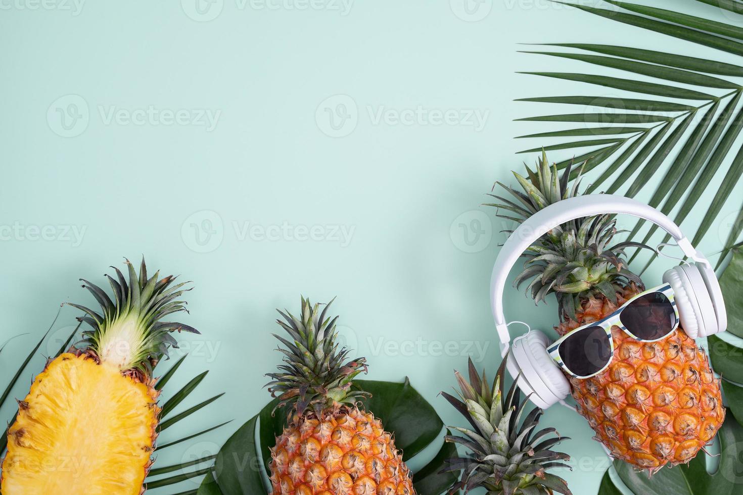 Funny pineapple wearing white headphone, concept of listening music, isolated on colored background with tropical palm leaves, top view, flat lay design. photo