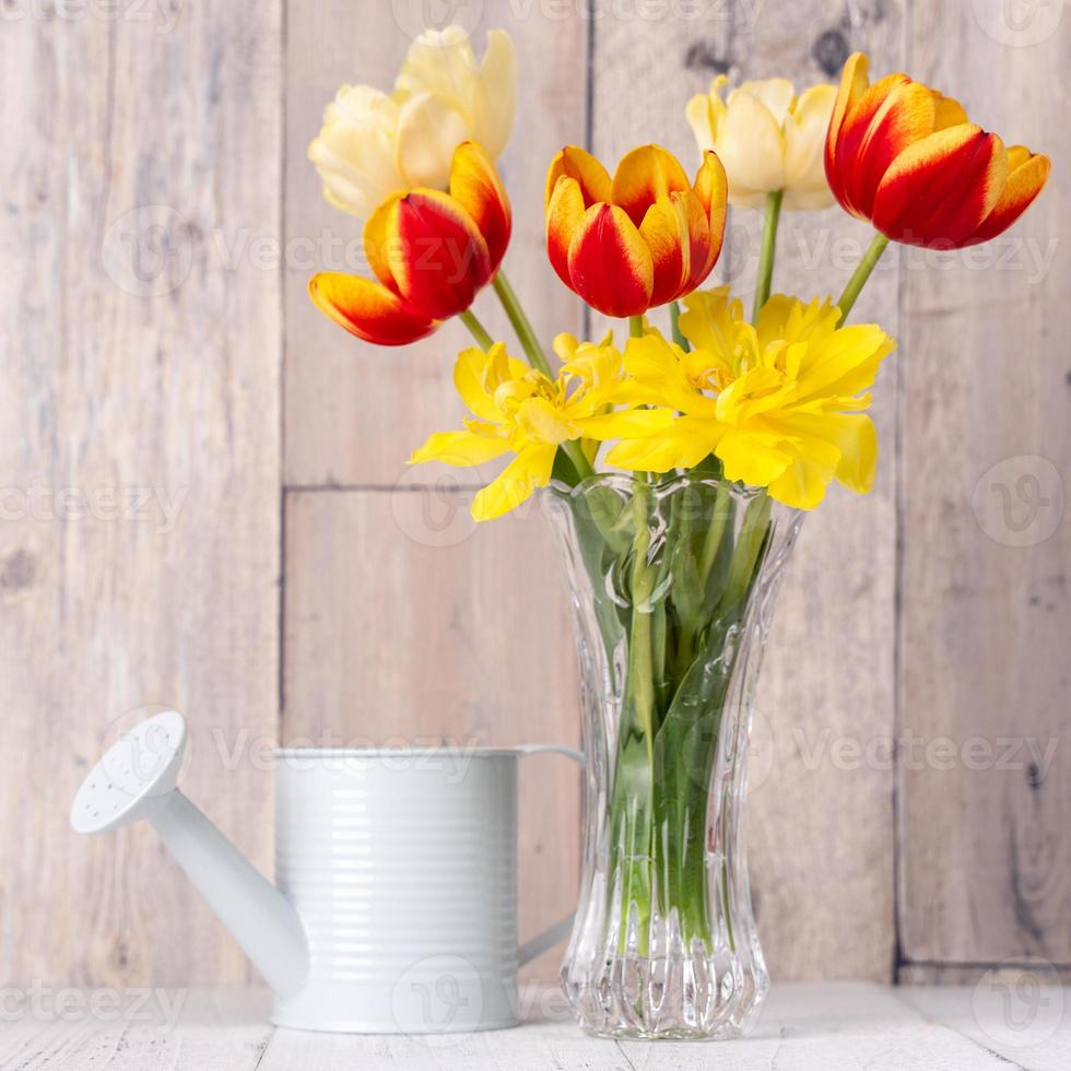 arreglo de flores de tulipán en jarrón de vidrio con saludo de corazón, decoración de latas de riego en la pared de fondo de la mesa de madera, primer plano, concepto de diseño del día de la madre. foto