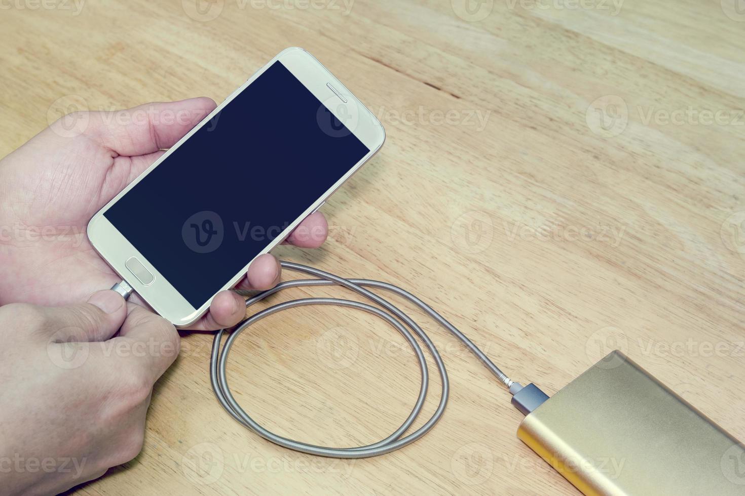 Smartphone charging in hand with power bank on wood background,filter effect photo