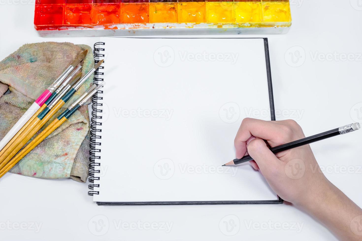 mano humana sosteniendo un lápiz con un cuaderno y una bandeja de colores foto