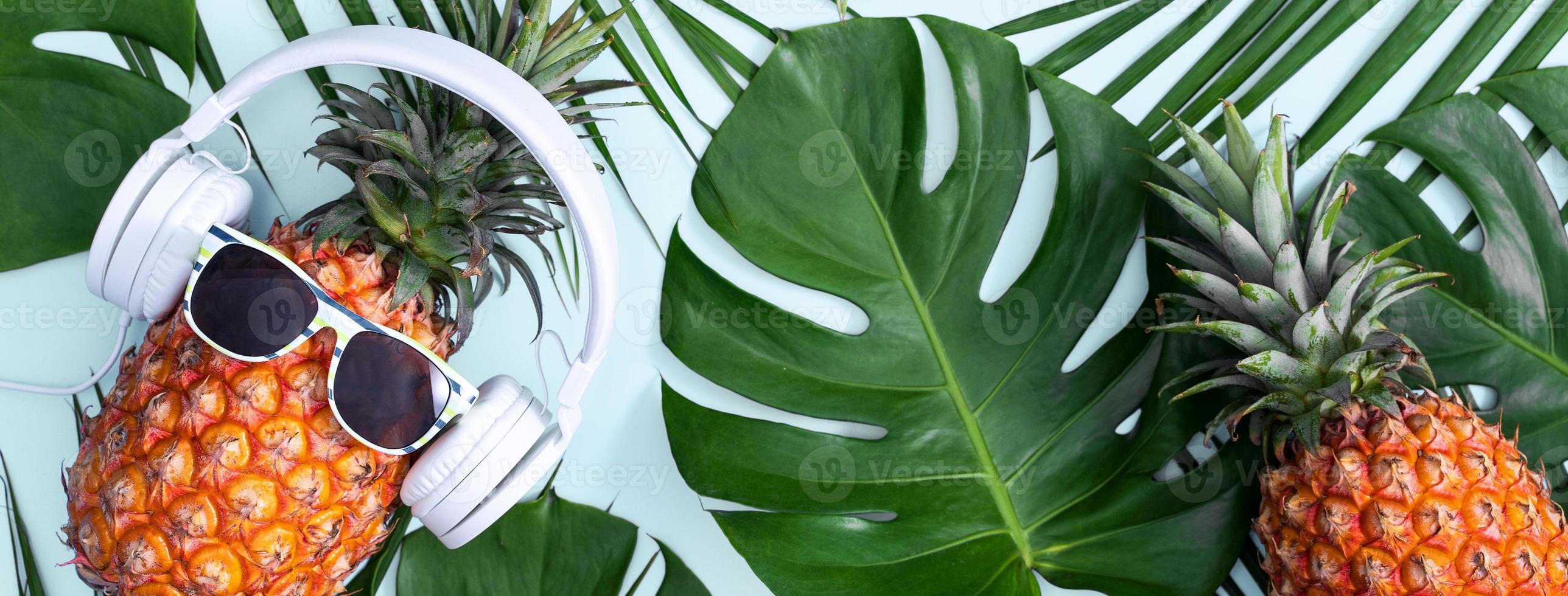 piña divertida con auriculares blancos, concepto de escuchar música, aislada en un fondo de color con hojas de palma tropical, vista superior, diseño plano. foto