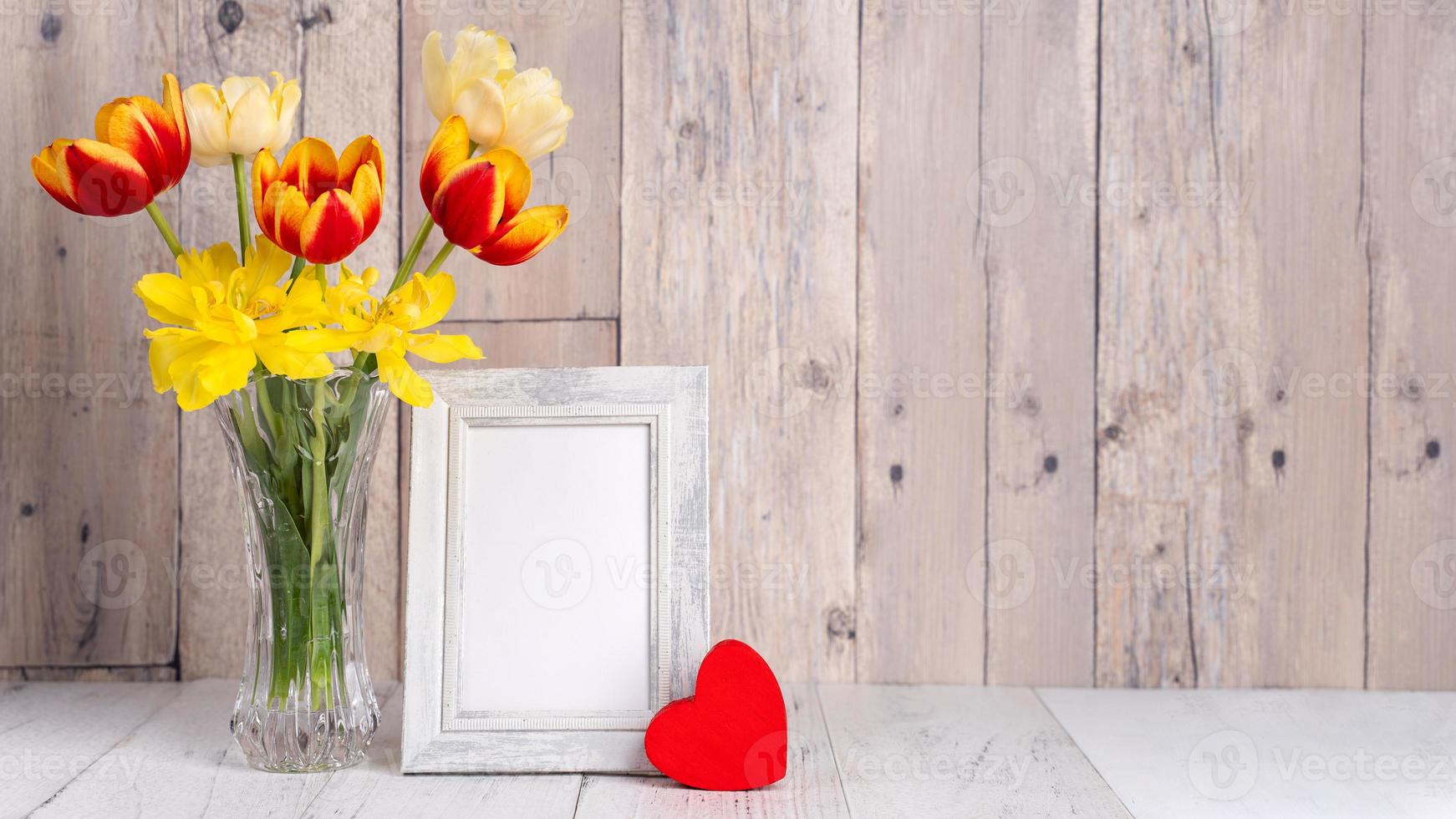 Tulip flower arrangement in glass vase with heart greeting, watering can decor on wooden table background wall, close up, Mother's Day design concept. photo