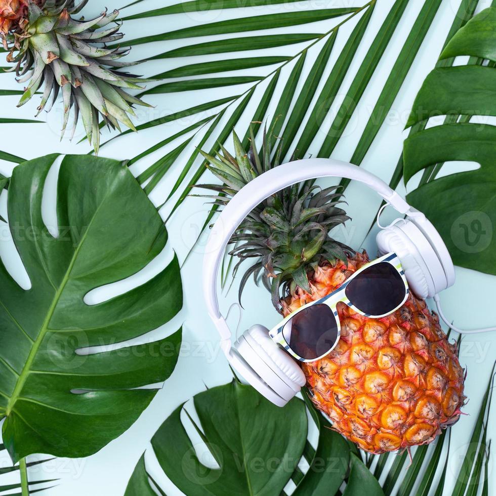 piña divertida con auriculares blancos, concepto de escuchar música, aislada en fondo azul con hojas de palma tropical, vista superior, diseño plano. foto