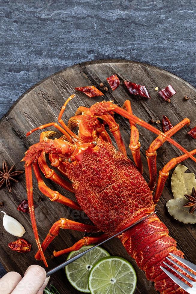 Cooked boiled lobster, delicious dinner seafood meal set with knife and fork on black stone slate background, restaurant menu design, top view, overhead photo