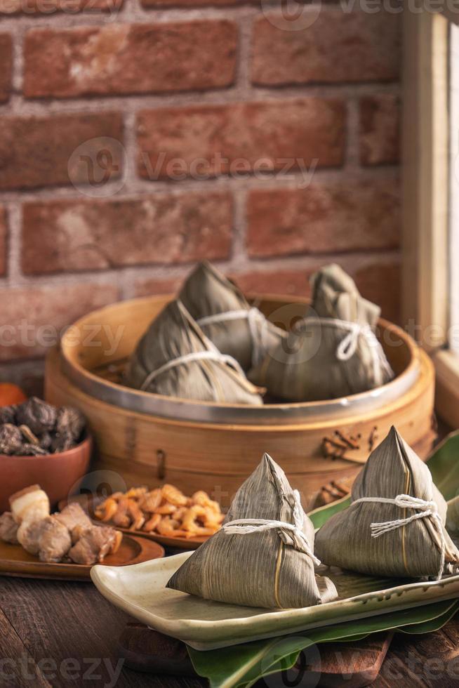 Rice dumpling, zongzi - Chinese rice dumpling zongzi in a steamer on wooden table with red brick, window background at home for Dragon Boat Festival concept, close up. photo