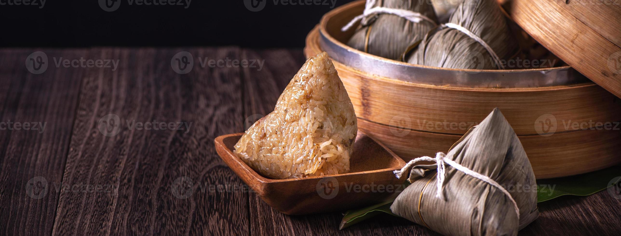 zongzi - bola de masa hervida de arroz chino zongzi en un vapor sobre una mesa de madera fondo retro negro para la celebración del festival del bote del dragón, primer plano, espacio de copia. foto