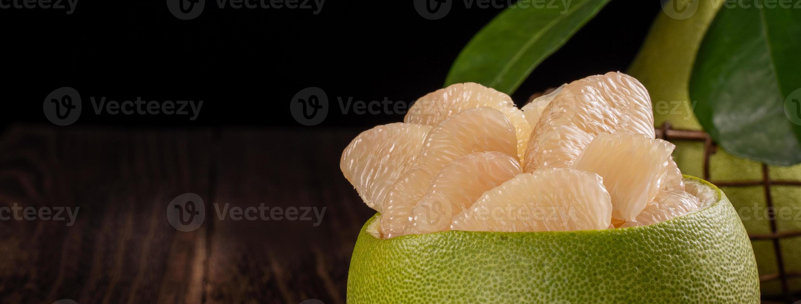 Fresh pomelo, pummelo, grapefruit, shaddock on wooden table over black background, close up, copy space. Fruit for Mid-autumn festival. photo