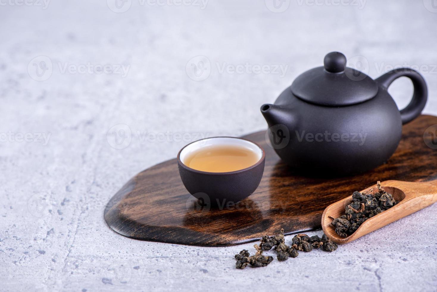 Hot tea in black teapot and cups and dry tea leaves over bright gray cement background, close up, copy space design concept. photo