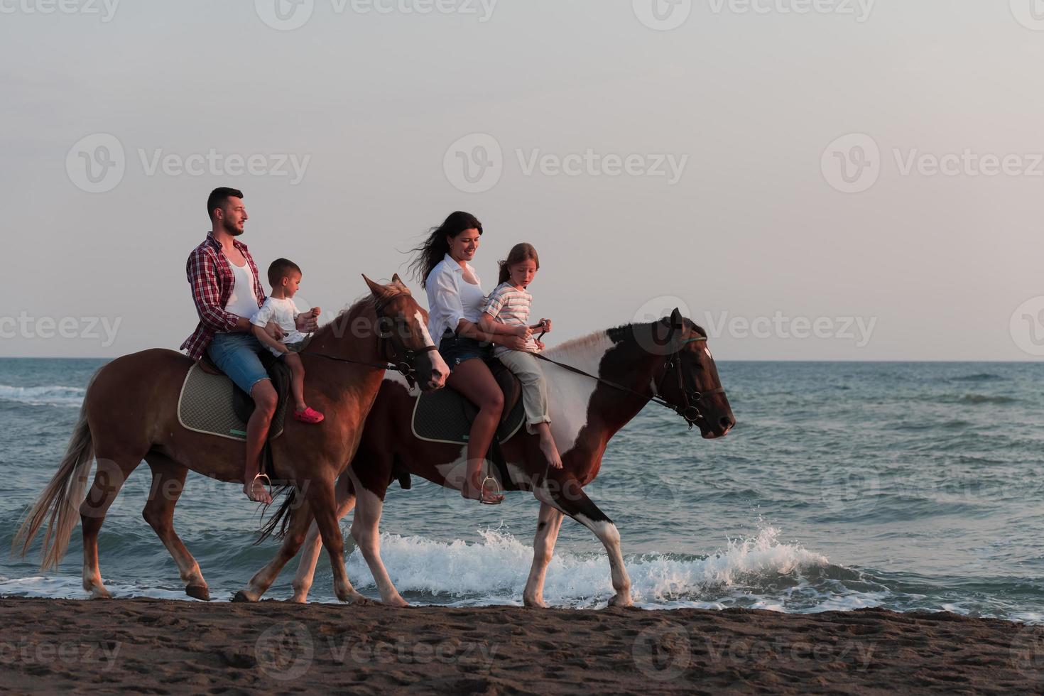 The family spends time with their children while riding horses together on a sandy beach. Selective focus photo