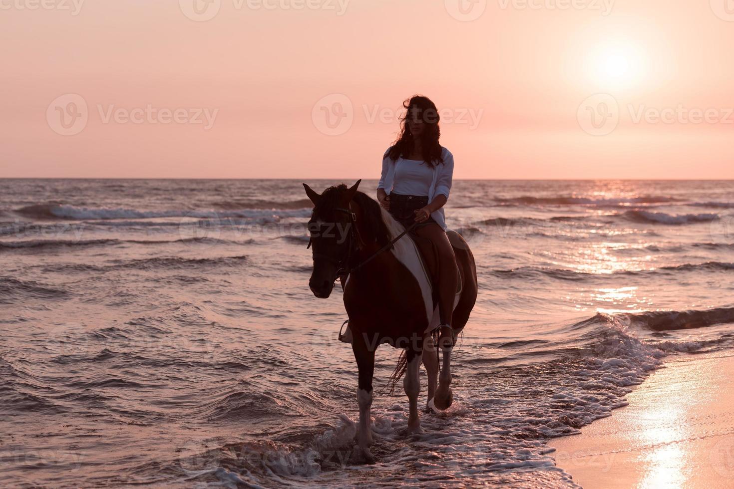 mujer vestida de verano disfruta montando a caballo en una hermosa playa de arena al atardecer. enfoque selectivo foto