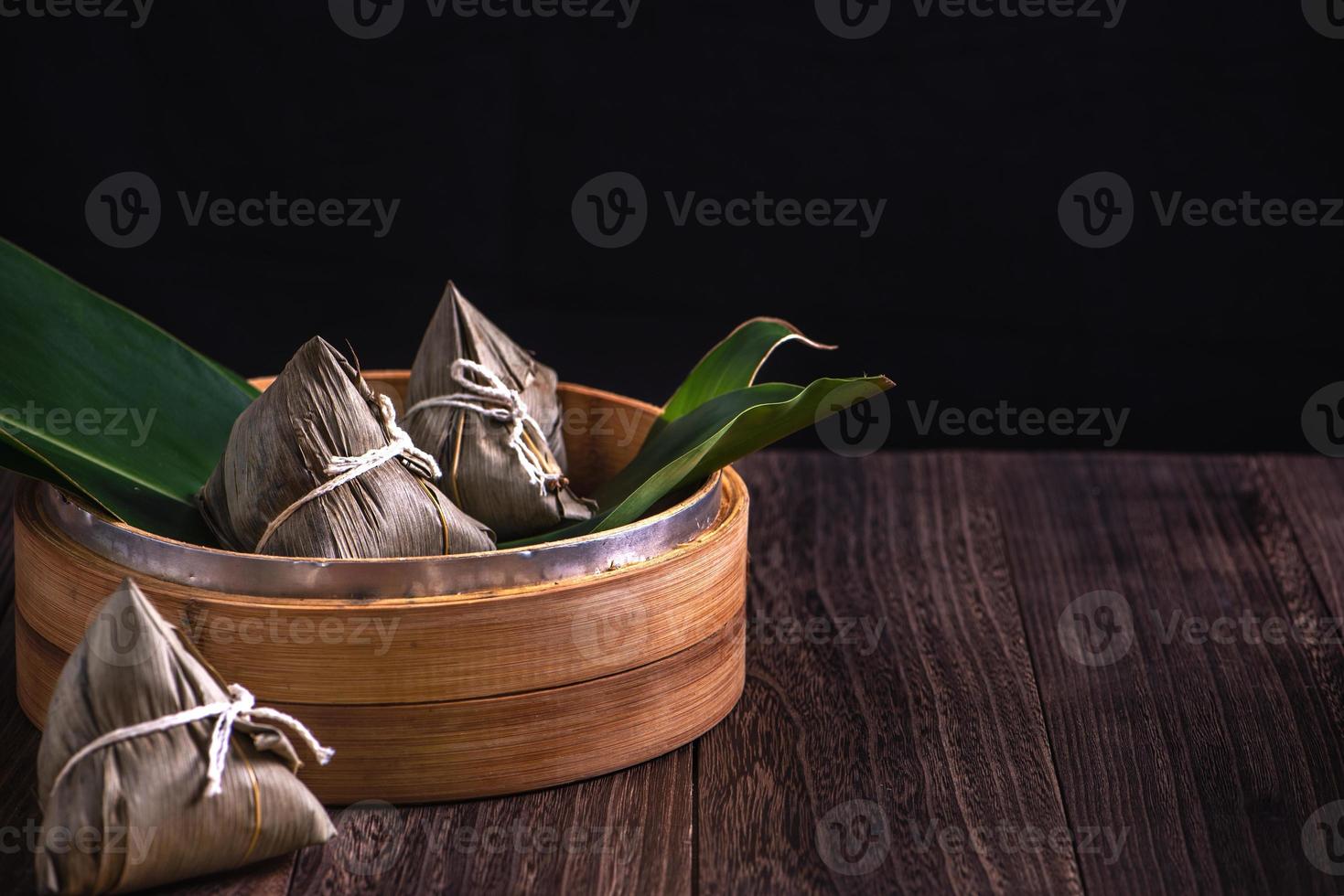 zongzi - bola de masa hervida de arroz chino zongzi en un vapor sobre una mesa de madera fondo retro negro para la celebración del festival del bote del dragón, primer plano, espacio de copia. foto