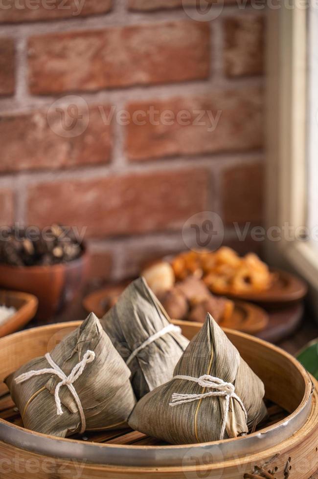 Zongzi - Chinese rice dumpling zongzi in a steamer on wooden table with red brick, window background at home for Dragon Boat Festival concept, close up. photo