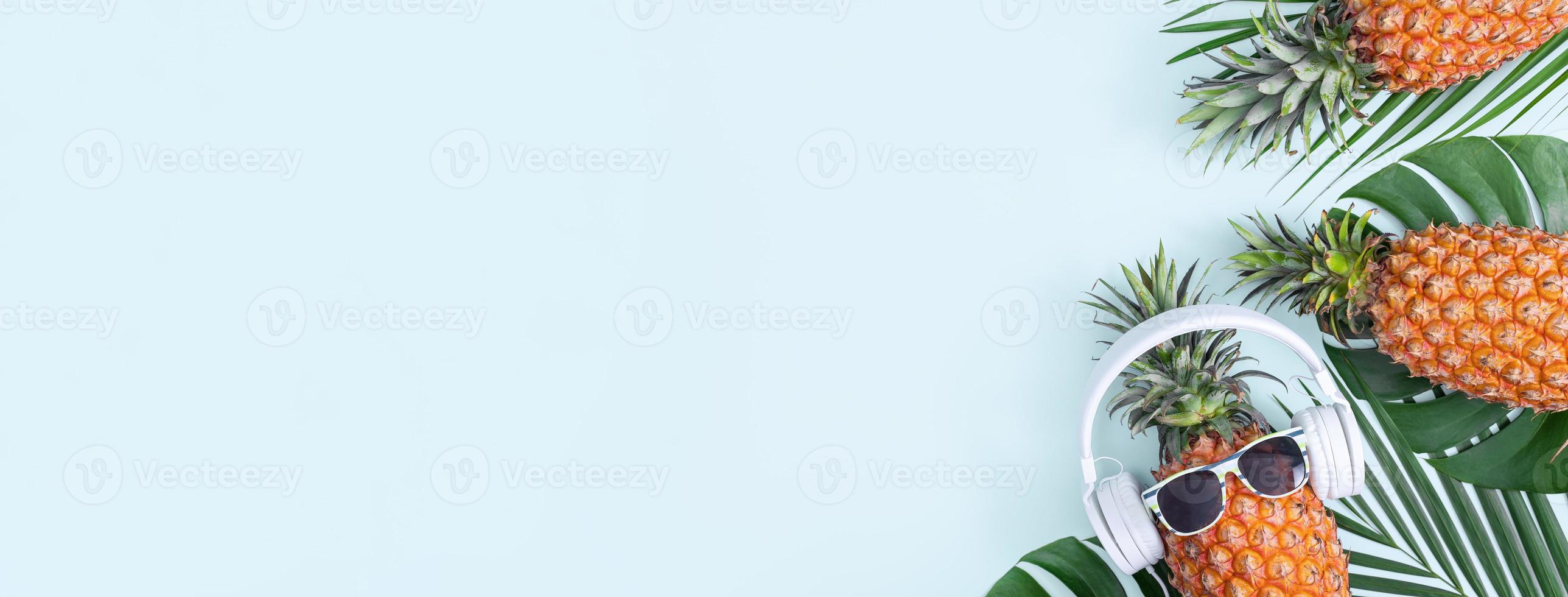 Funny pineapple wearing white headphone, concept of listening music, isolated on colored background with tropical palm leaves, top view, flat lay design. photo