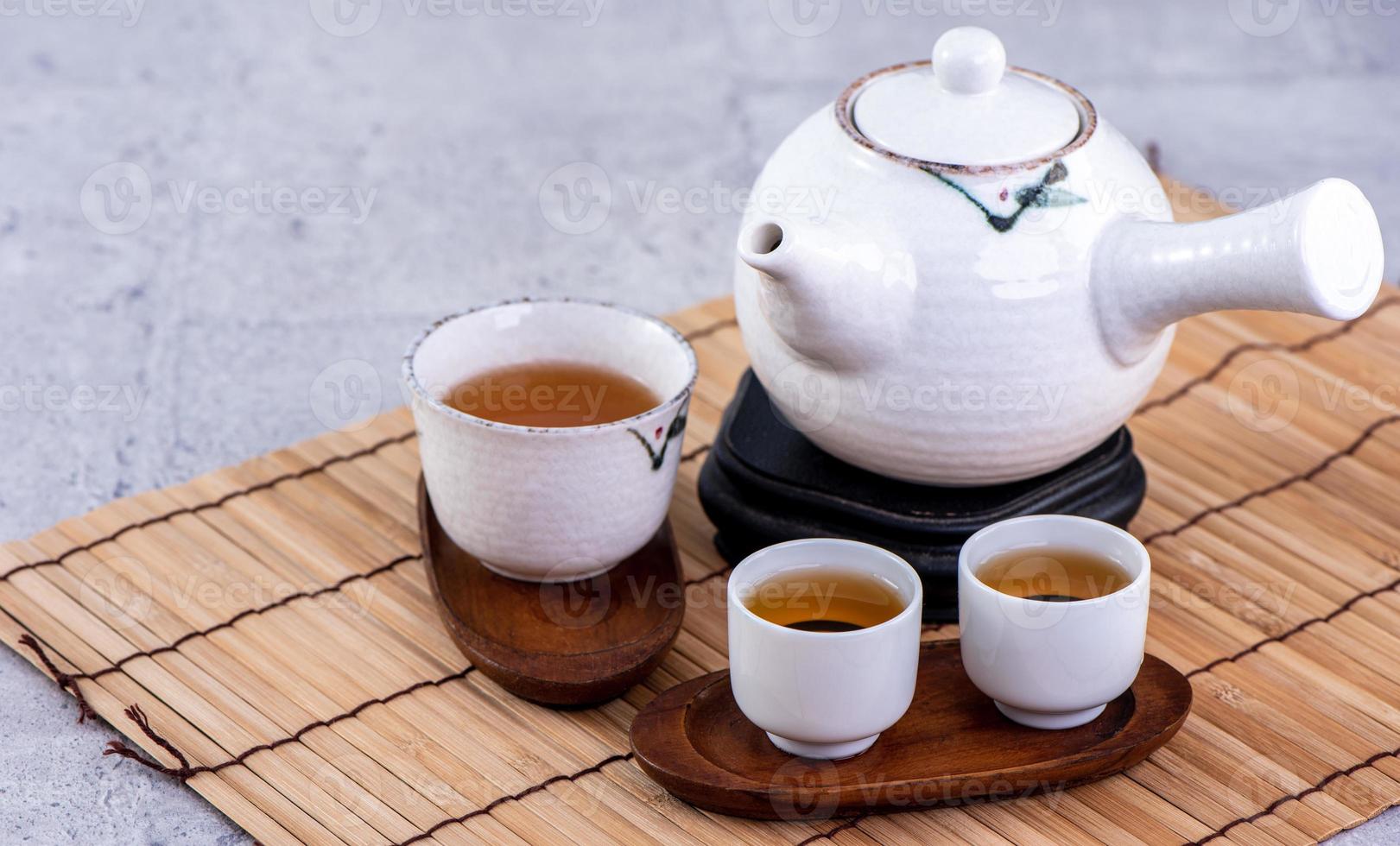 Hot tea in white teapot and cups on a sieve over bright gray cement background, closeup, copy space design concept. photo