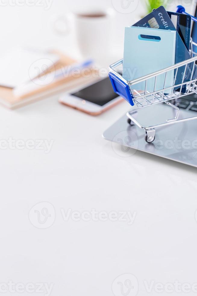Office online paying, stay home shopping, electronic payment with credit card concept, laptop on white table background with shop cart, close up. photo