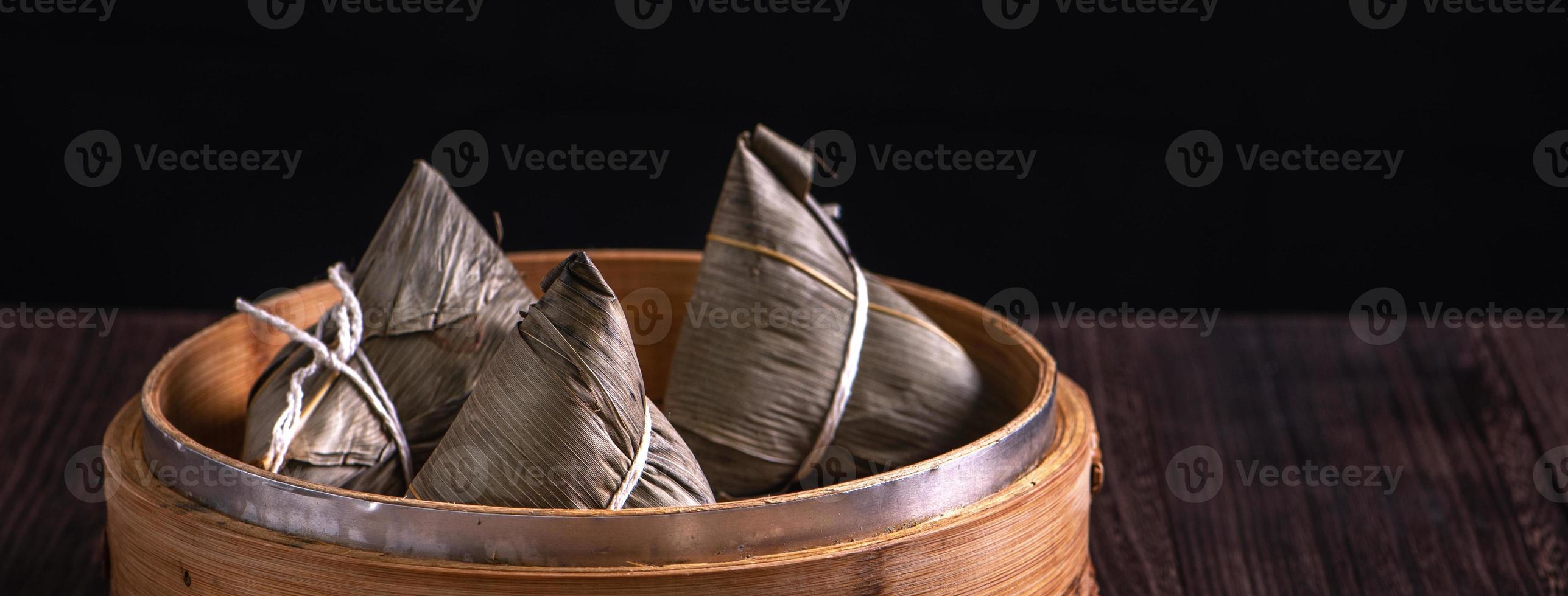 bola de arroz, zongzi - montón de comida tradicional china cocinada en una mesa de madera sobre fondo negro, concepto de festival de botes de dragón, primer plano, espacio de copia foto