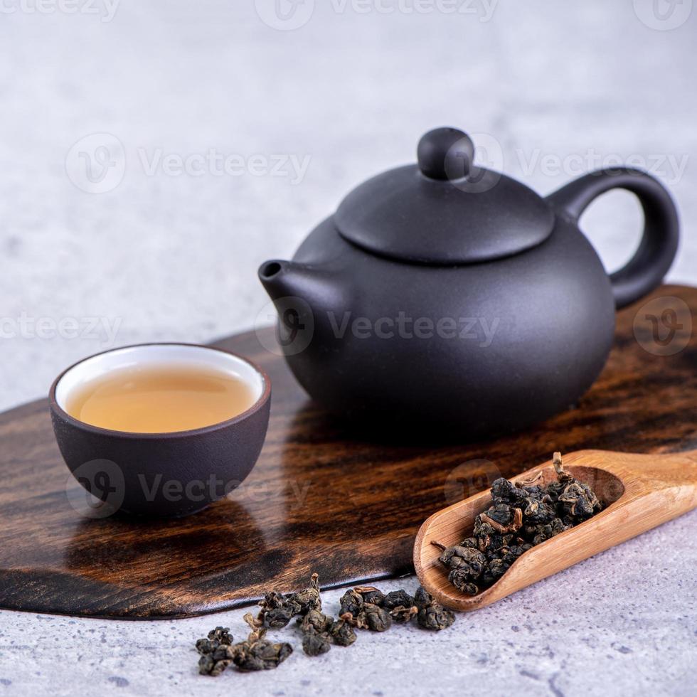 Hot tea in black teapot and cups and dry tea leaves over bright gray cement background, close up, copy space design concept. photo