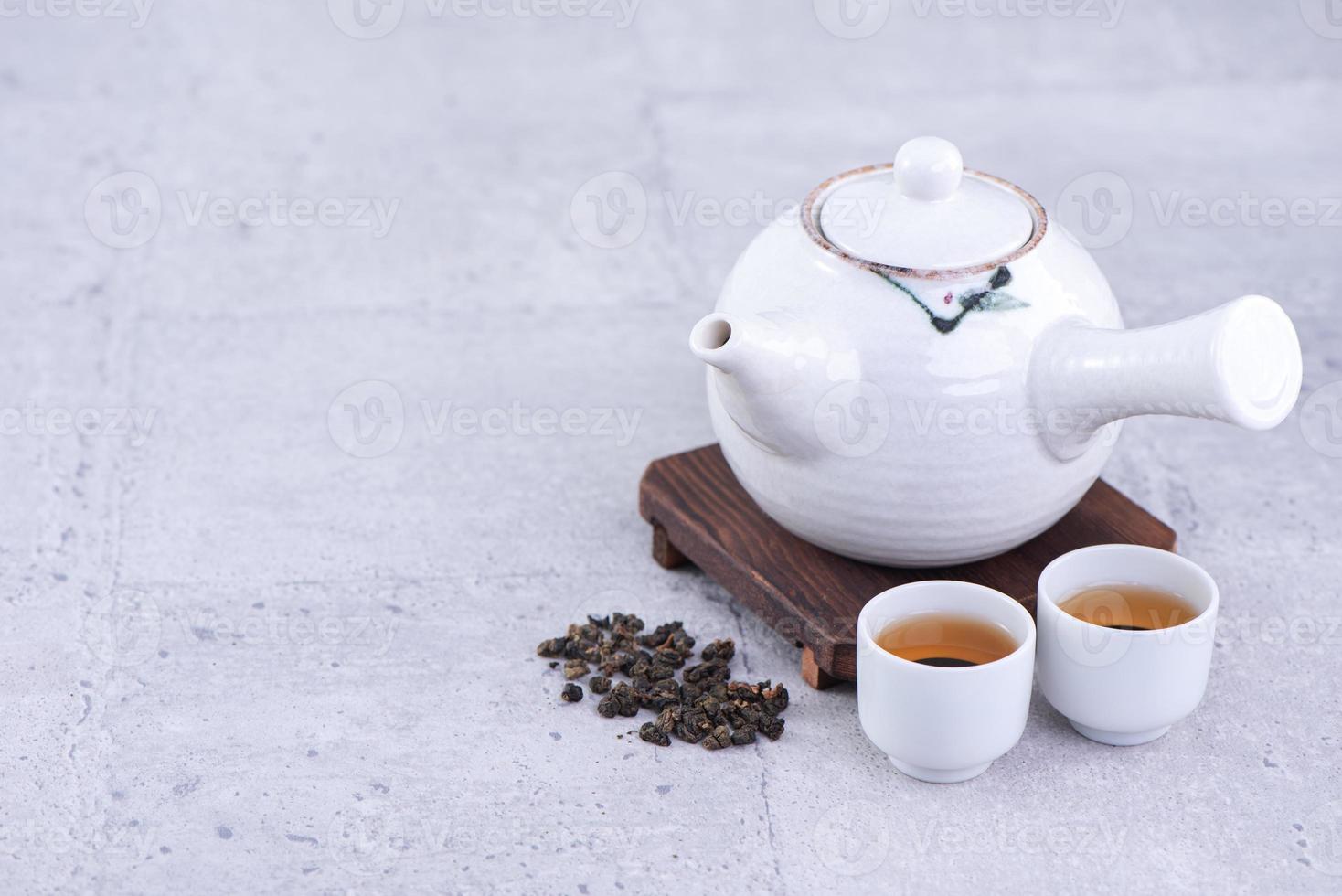 Hot tea in white teapot and cups on a sieve over bright gray cement background, closeup, copy space design concept. photo