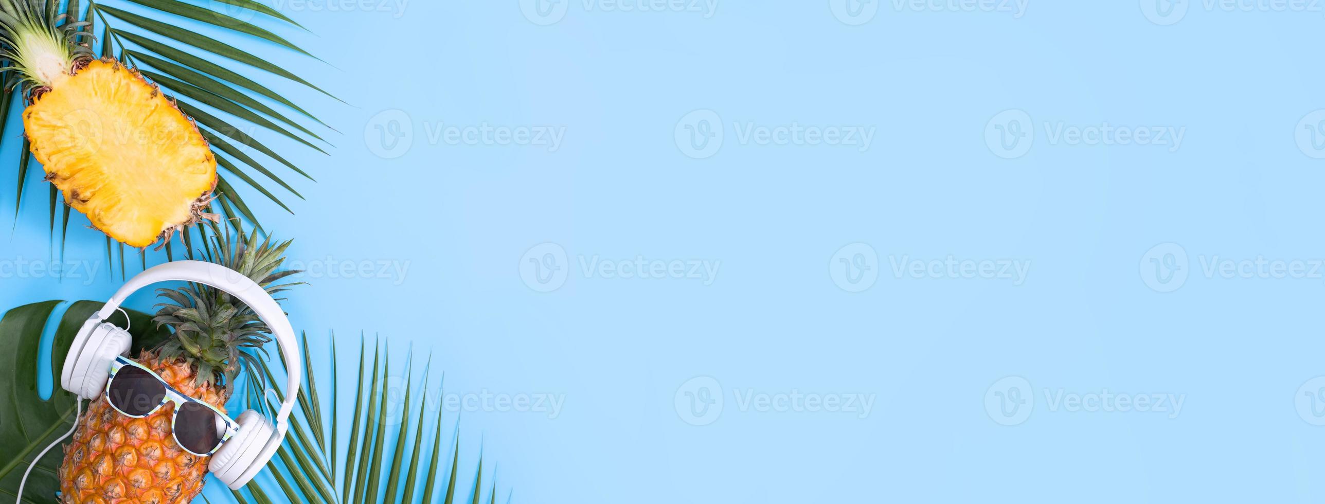 Funny pineapple wearing white headphone, concept of listening music, isolated on colored background with tropical palm leaves, top view, flat lay design. photo