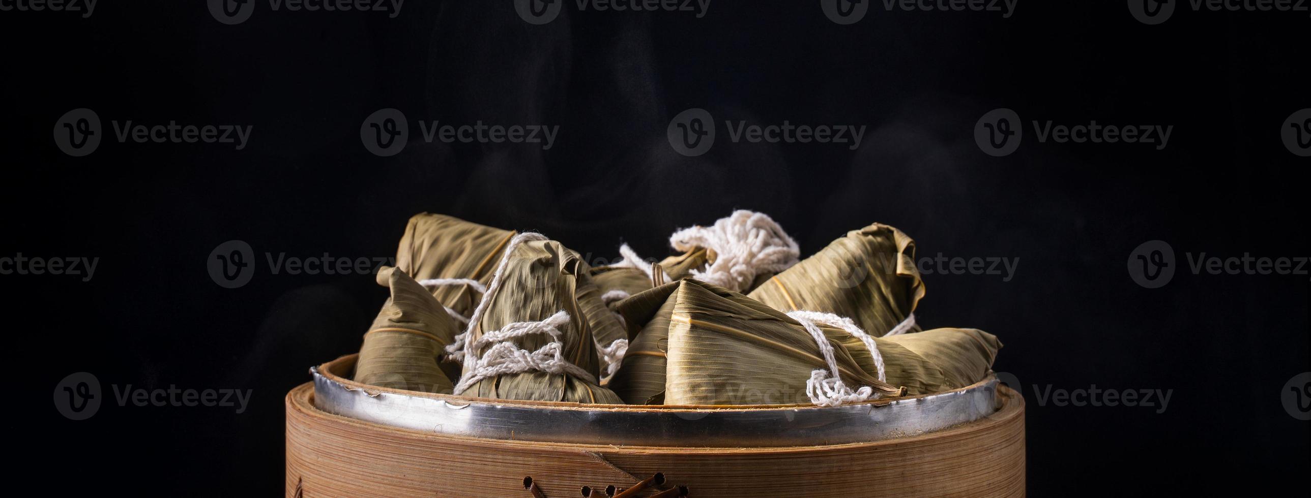 Rice dumpling, zongzi - Dragon Boat Festival, Bunch of Chinese traditional cooked food in steamer on wooden table over black background, close up, copy space photo