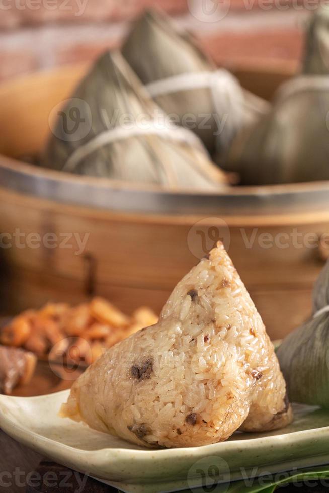 dumpling de arroz - comida china zongzi en un vapor sobre una mesa de madera con pared de ladrillo rojo, fondo de ventana en casa para el concepto del festival del bote del dragón, de cerca. foto