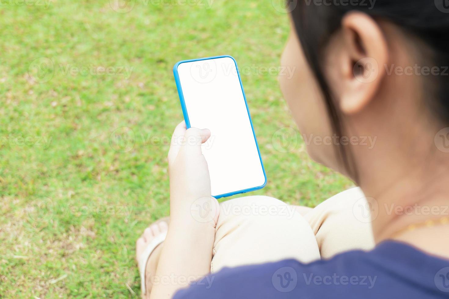 Taken from behind, across the shoulder of a blurry Asian woman. But clearly the mobile phone that cuts the screen to white Social media in the park photo