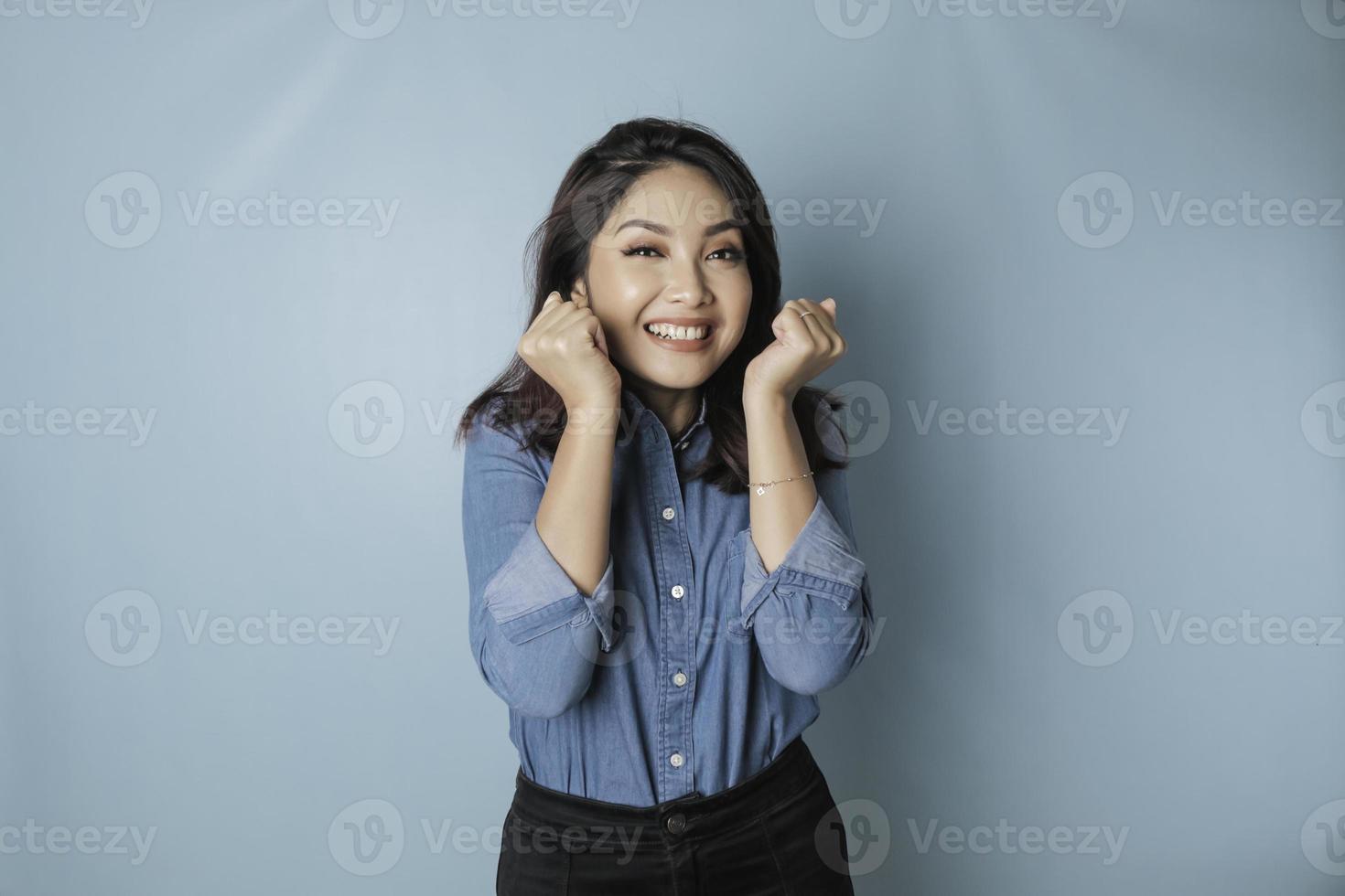 A portrait of a cute Asian woman wearing a blue shirt and feeling excited and isolated by a blue background photo