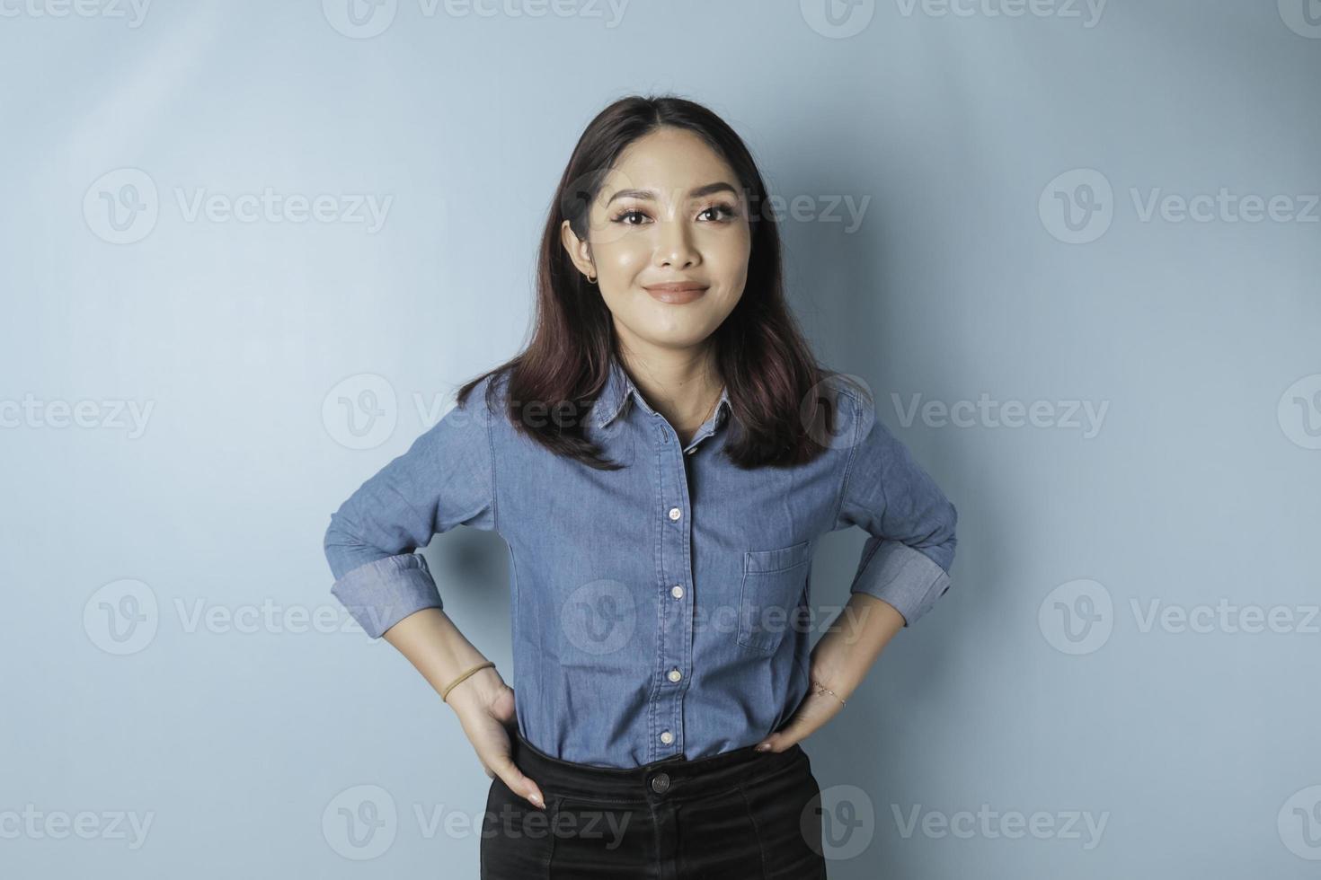 Portrait of a confident smiling girl standing with arms folded and looking at the camera isolated over blue background, wearing a blue shirt photo