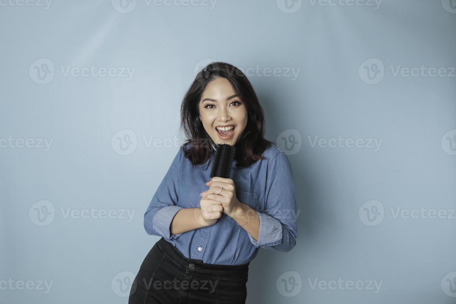 Portrait of carefree Asian woman, having fun karaoke, singing in microphone while standing over blue background photo